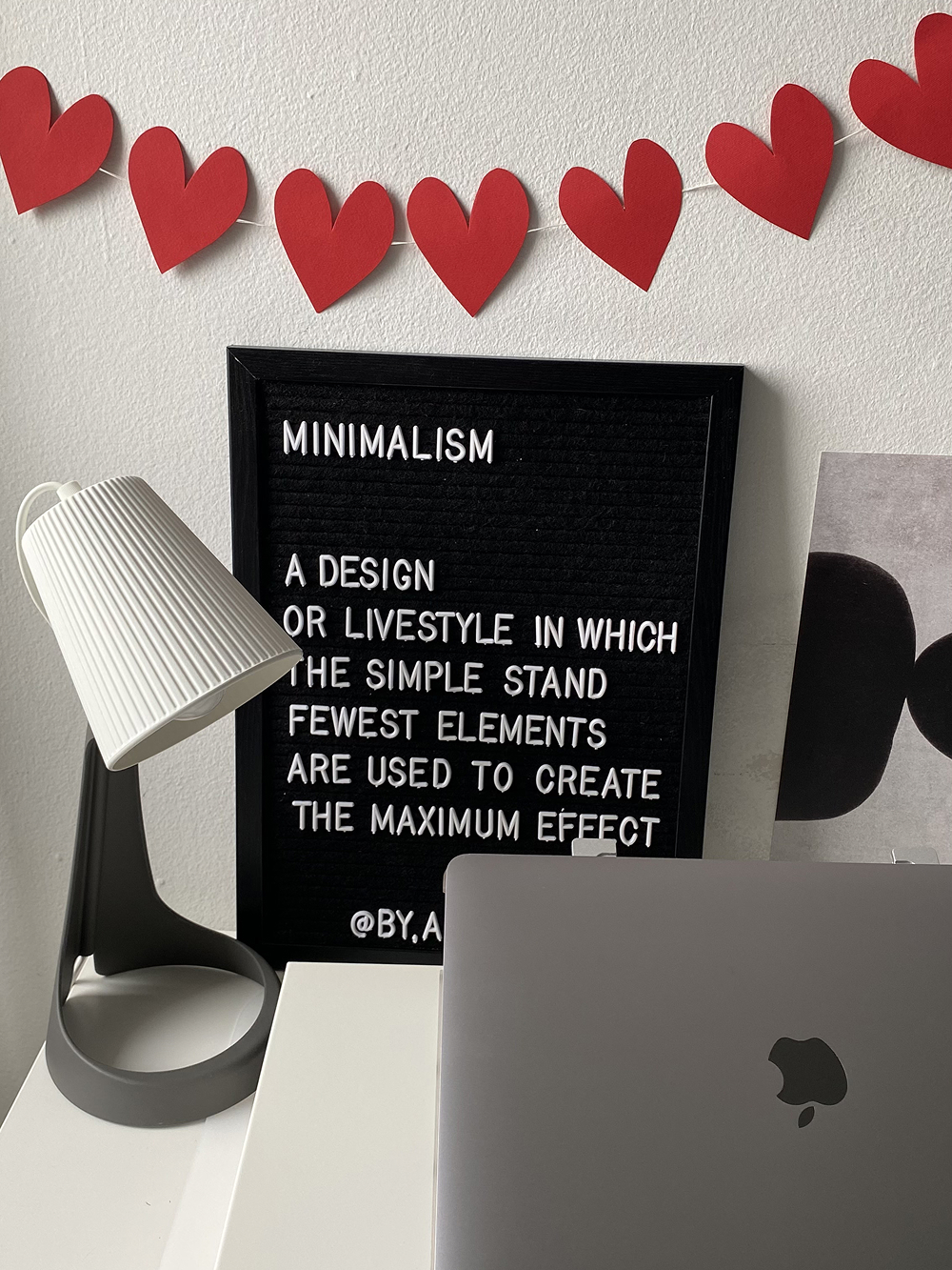 There is a picture of letters, a table lamp and a MacBook on the table.