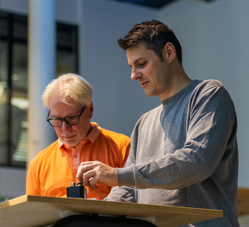 Zwei Männer arbeiten zusammen an einem technischen Gerät auf einem Tisch.