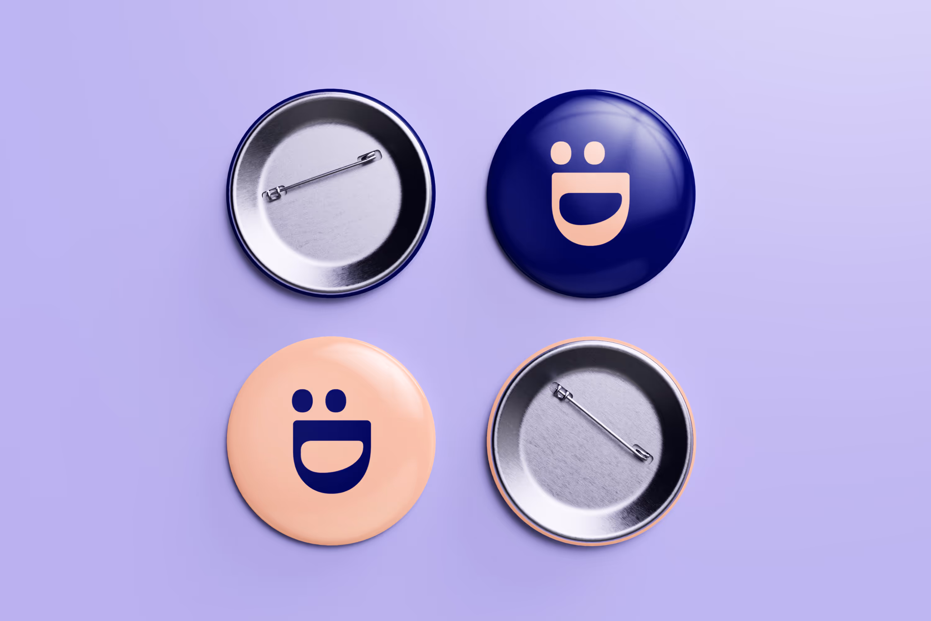 Four round pinback buttons on a purple surface, two with smiling face designs in contrasting colors and two showing the metal pin backs.