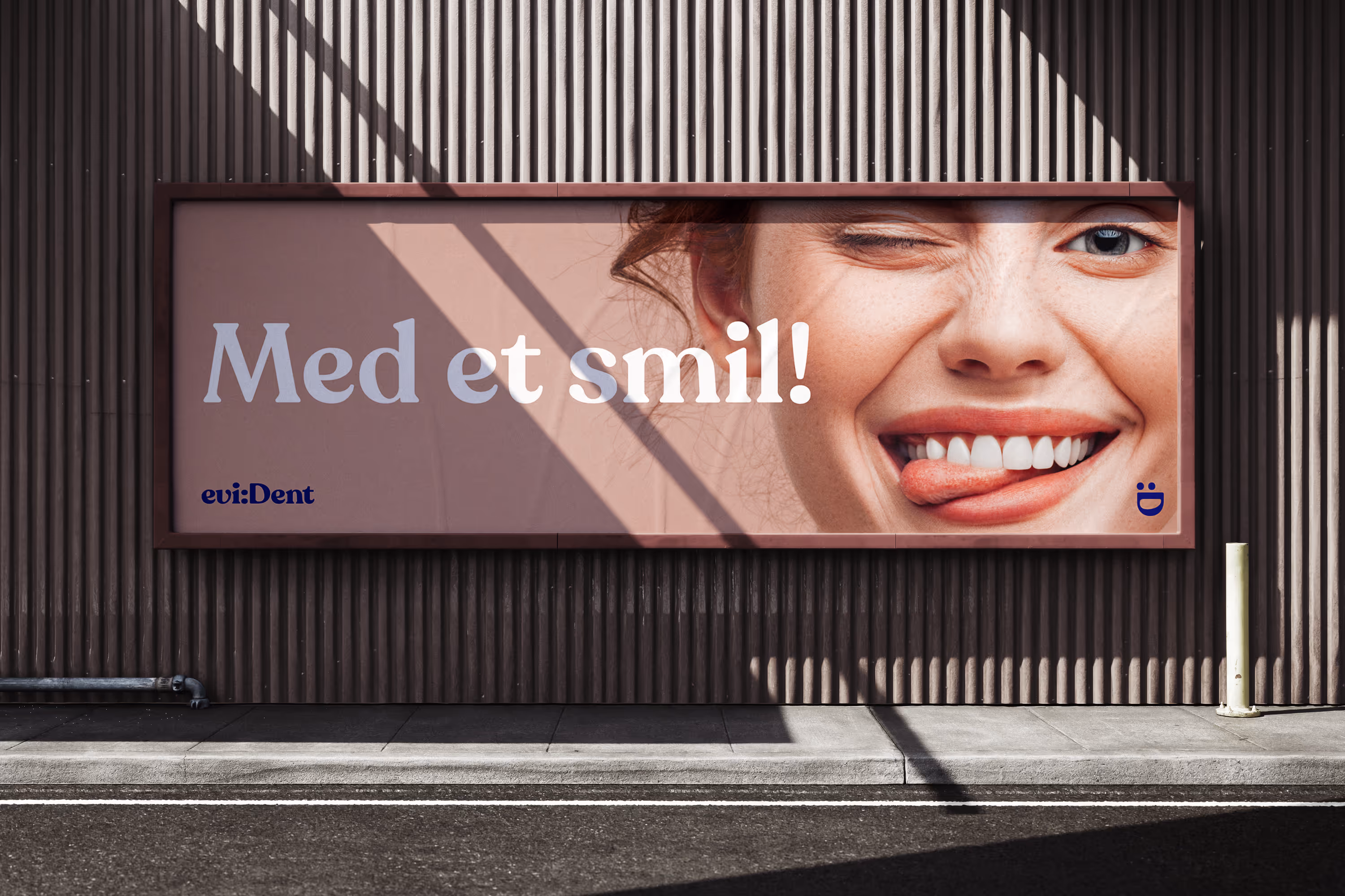 Outdoor billboard on a ribbed wall showing a close-up of a smiling woman winking and sticking out her tongue with the Norwegian text 'Med et smil!' meaning 'With a smile!'