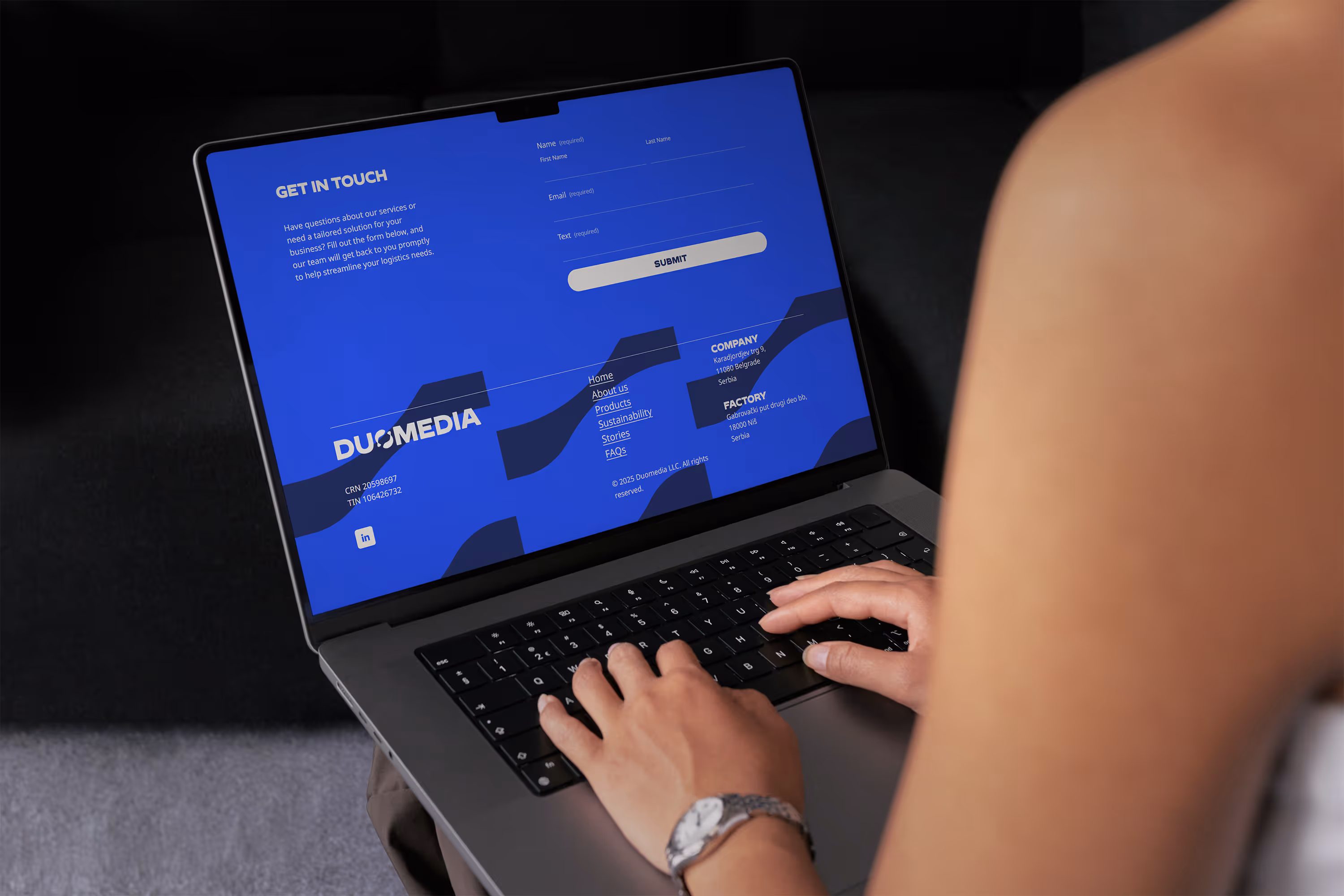 Person typing on a laptop showing a blue webpage with a contact form and a footer section with the company information for DUOMEDIA.