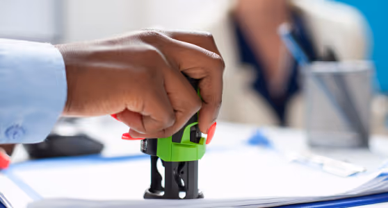 Person holding a green self-inking stamp pressing down on documents on a desk.
