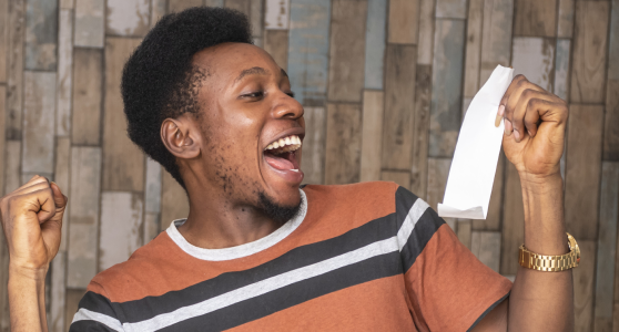 Excited young man in striped shirt holding and looking at a blank receipt or ticket with a joyful expression.