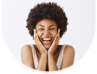 Smiling woman with curly hair holding her face with both hands against a white background.