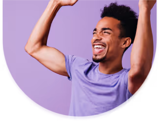 Smiling young man with raised arms wearing a purple shirt against a purple background.