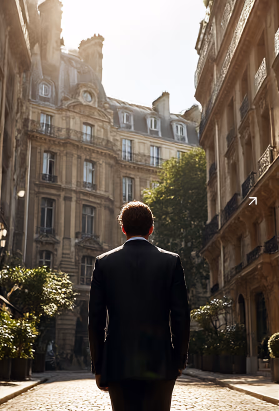 Un homme en costume noir vu de dos marchant dans une rue pavée bordée de bâtiments haussmanniens sous un ciel lumineux.