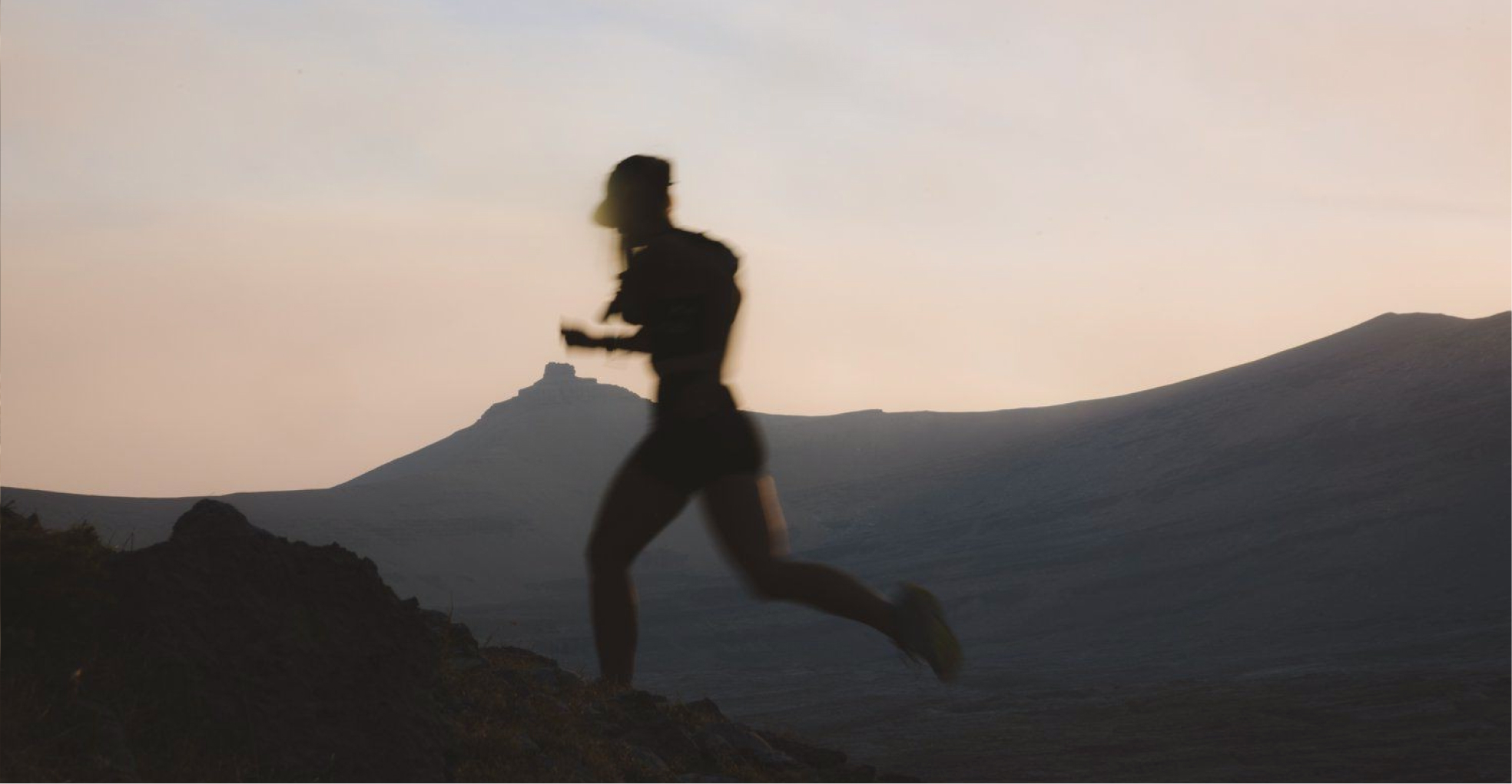 Silhouette of a person running uphill at dusk with mountains in the background.