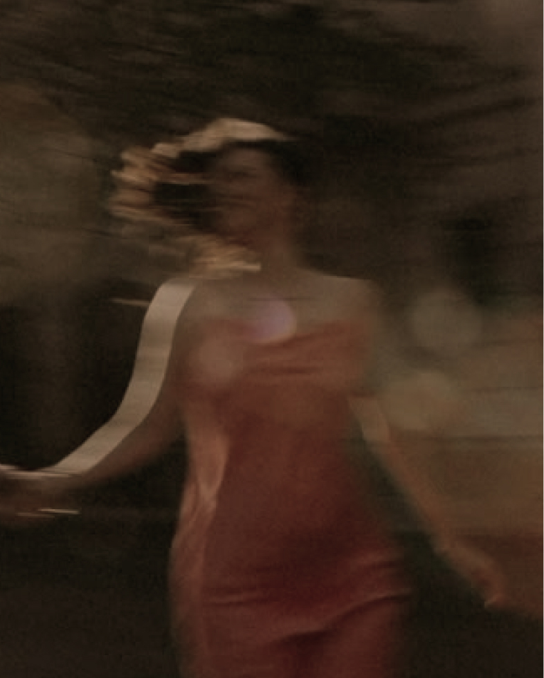 Blurred image of a person in a reddish dress moving in a dark setting with light reflections.
