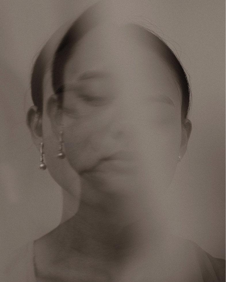 Blurred double exposure portrait of a woman with closed eyes and earrings in muted tones.