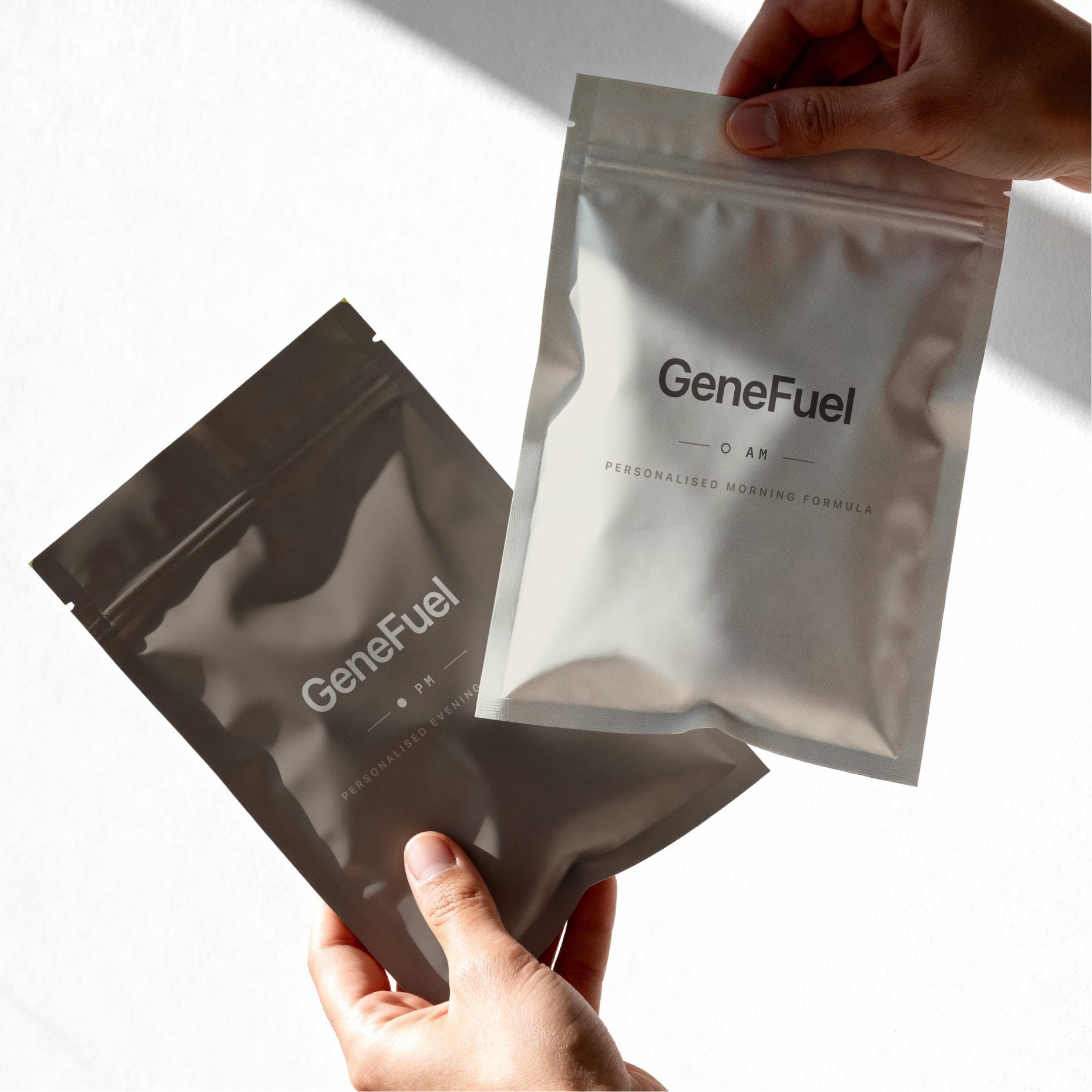 Two hands holding a grey and a light grey GeneFuel personalized supplement pouch for AM and PM.