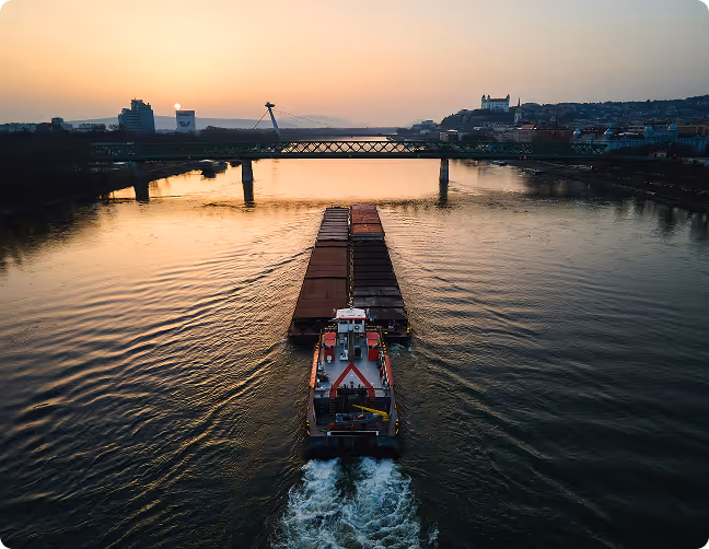 Large orange logging machinery loading long tree logs onto a stack beside a truck in a logging yard.
