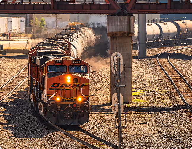 BNSF freight train with locomotive number 6224 traveling on railway tracks under a bridge on a sunny day.