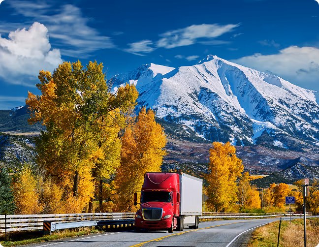 Log loader crane lifting long logs onto a large stacked pile next to a purple logging truck.