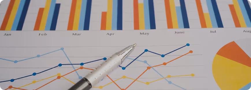 Pen pointing at a line graph with multiple colored lines and bar charts showing data trends from January to August.
