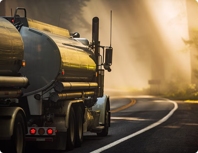 Large tanker truck driving on a winding road with sunlight filtering through fog.