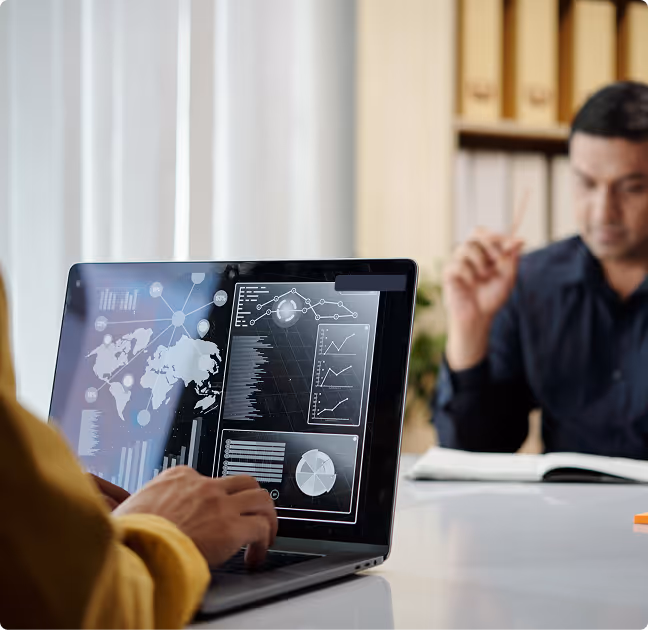Person working on a laptop displaying digital data visualizations including world map, graphs, and charts with another person blurred in the background.