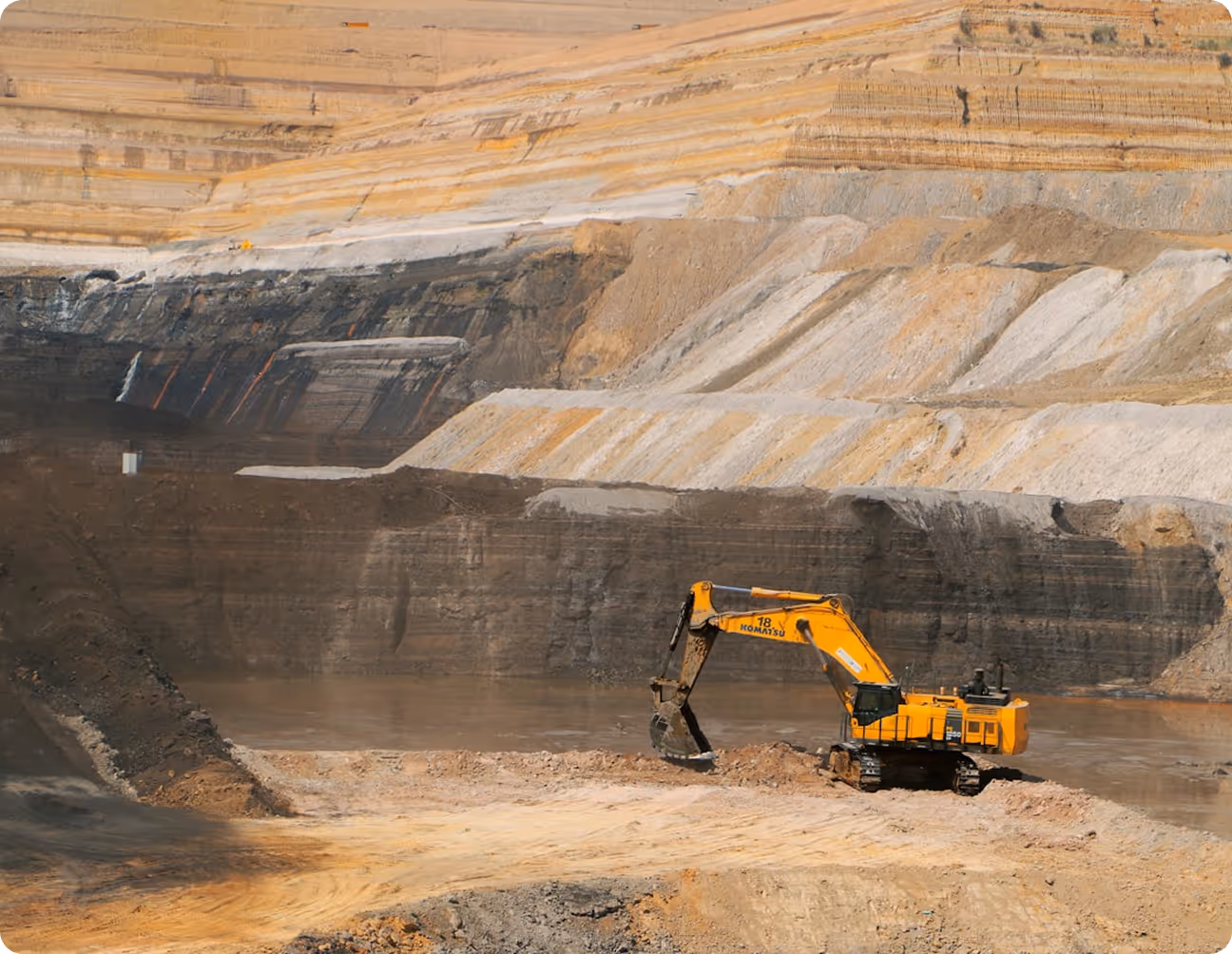 Yellow excavator digging at a multi-layered open-pit mine with terraced earth walls.