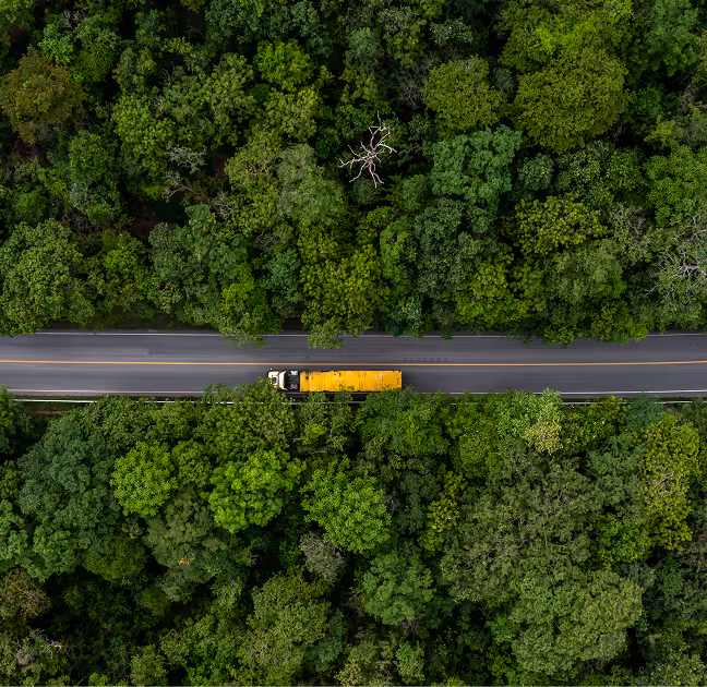 Two business professionals, a woman and a man, shaking hands in a warehouse with the man holding a clipboard with contract documents.
