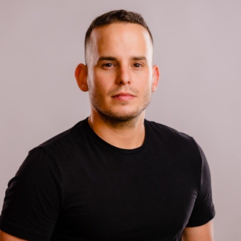 Man wearing a gray suit and light blue shirt against a plain gray background.