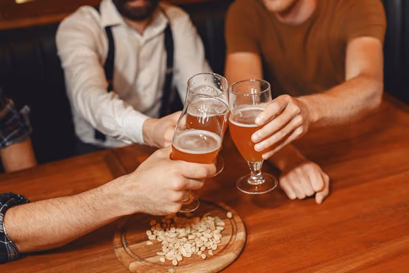 A wooden table with a tray of nuts and two glasses of beer.