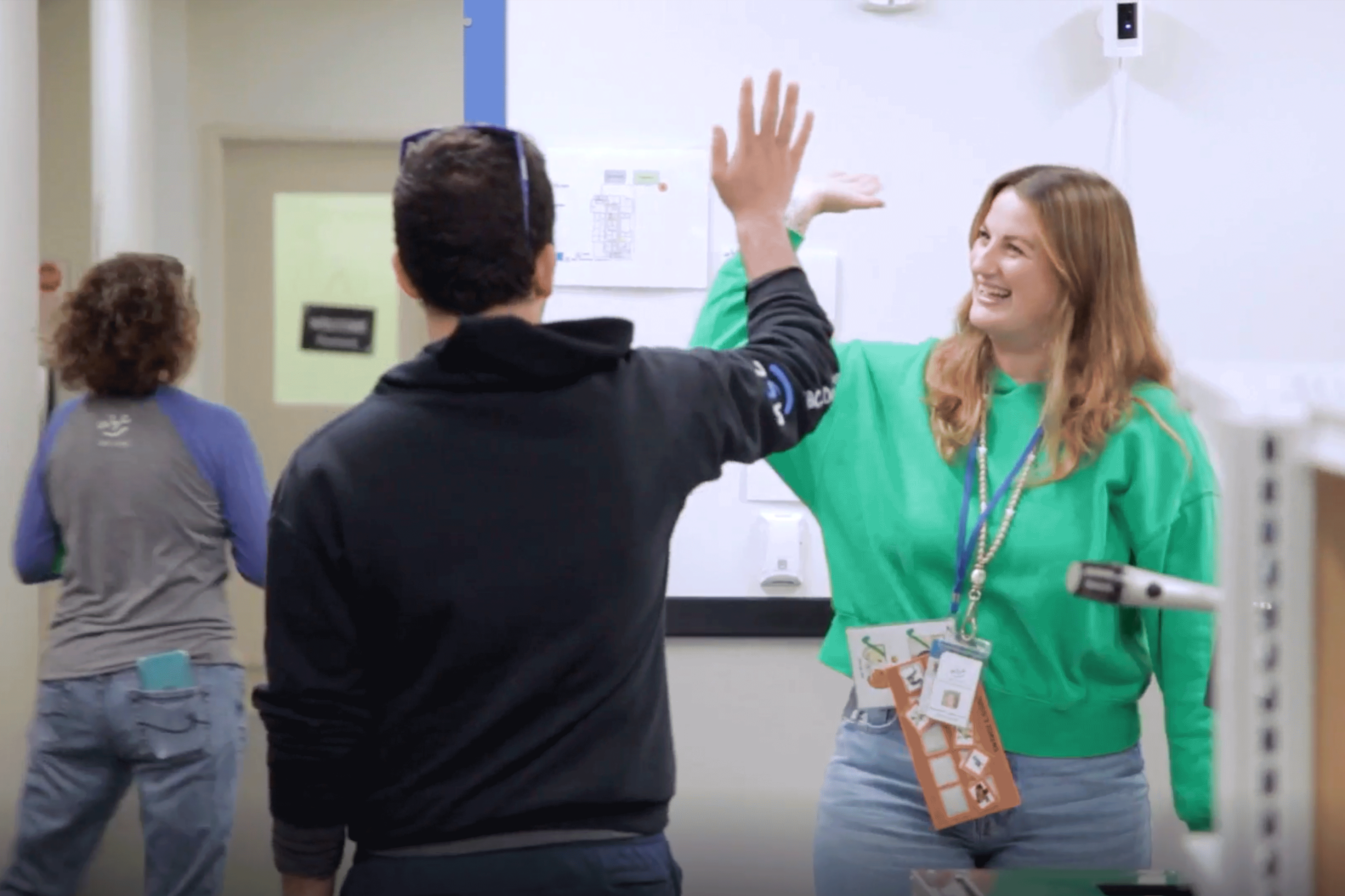 Two people giving a high five in a room while a third person walks away.
