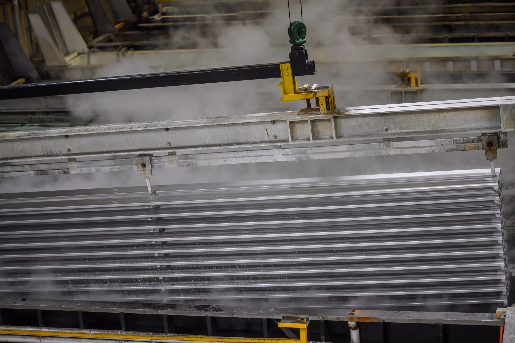 Industrial machinery with metal beams immersed in a steaming tank during anodizing process.