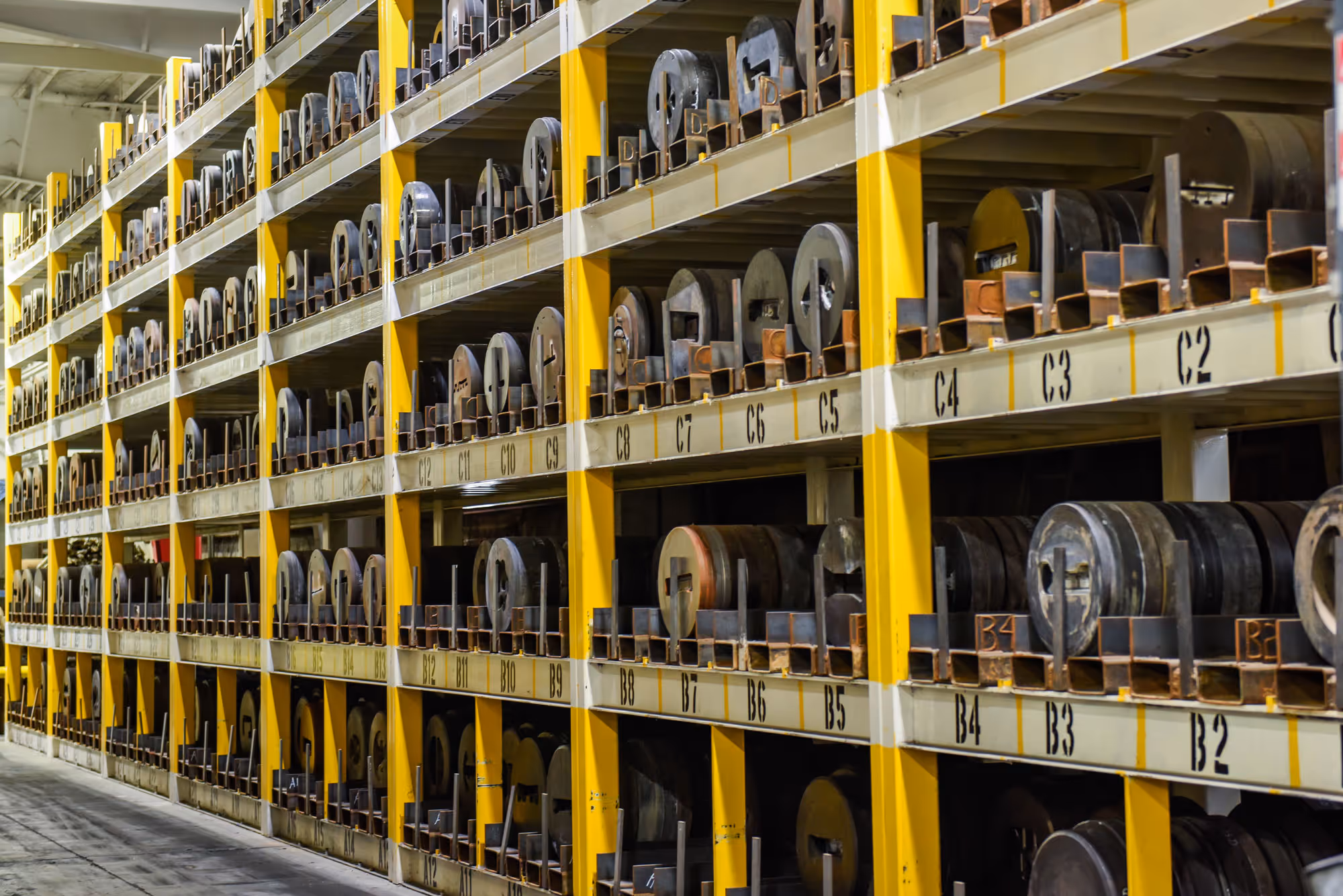 Industrial storage racks with multiple rows of large metal rollers organized and labeled in a warehouse.