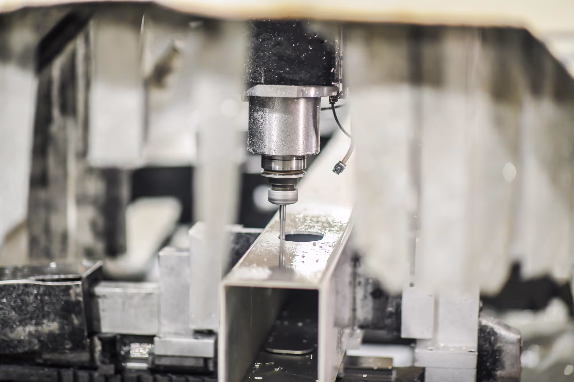 CNC milling machine drilling a rectangular metal tube with metal shavings around.