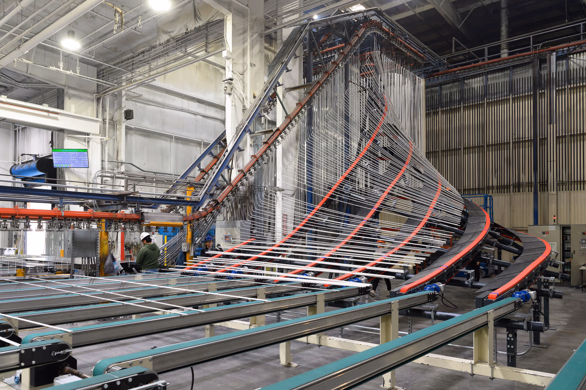 Modern industrial factory interior with large conveyor belts and machinery for material processing, workers operating in the background.