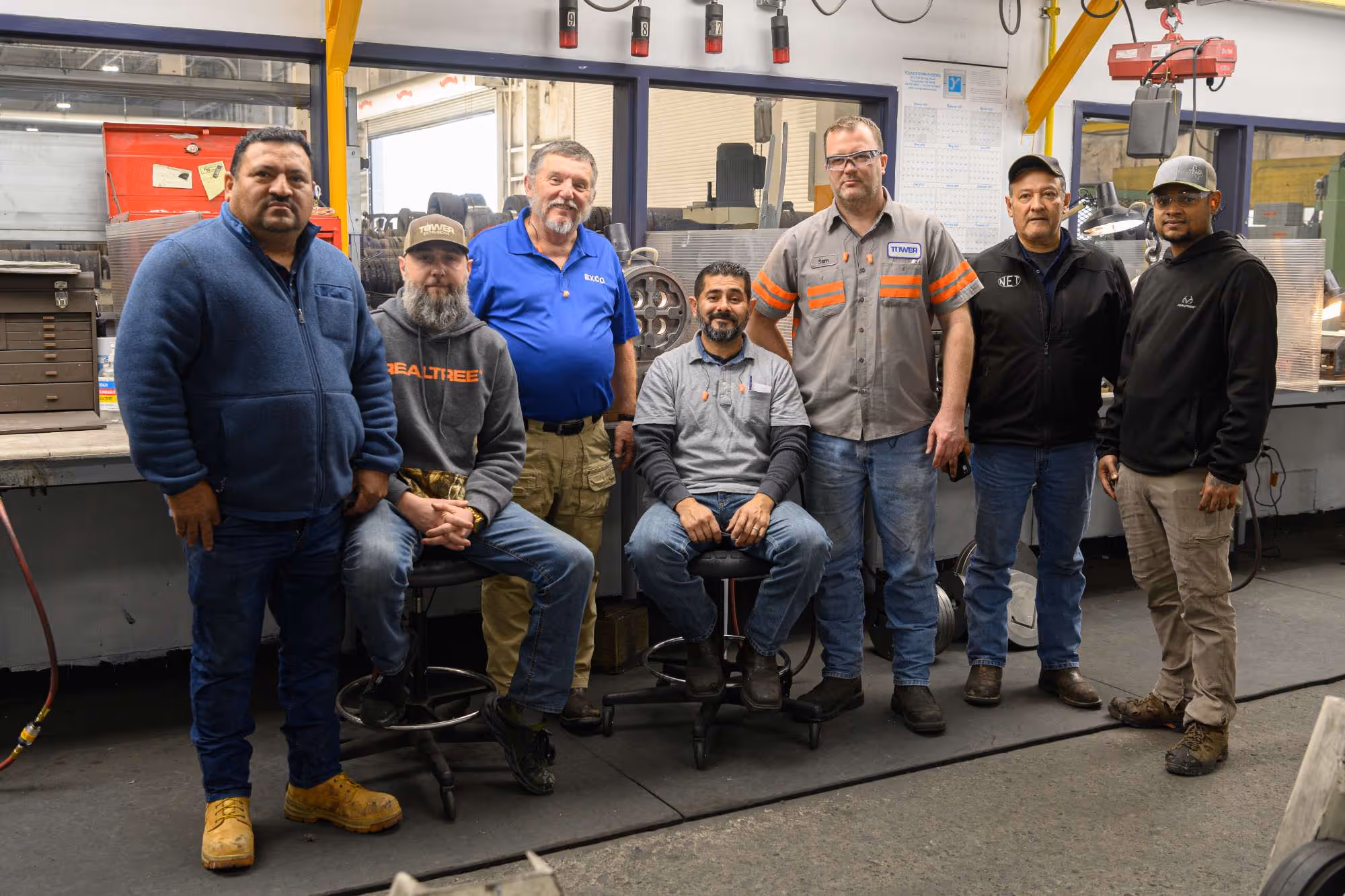 Group of seven men in casual and work attire posing inside an industrial workshop.