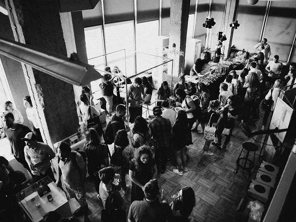 A large group of people gathered indoors at an event with booths and tables.