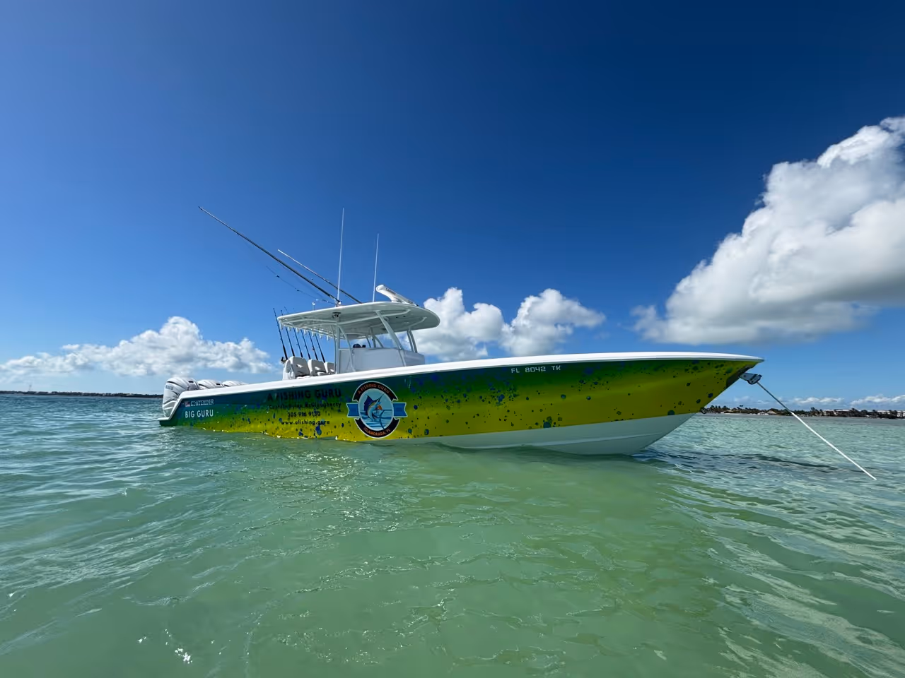 Fishing boat with yellow and green design anchored in clear turquoise water under a blue sky with scattered clouds.