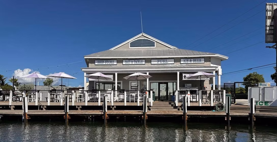 Waterfront IslaMarina marina with outdoor seating, umbrellas, and signs reading ship store, bait & tackle, fuel, and ice & beer.