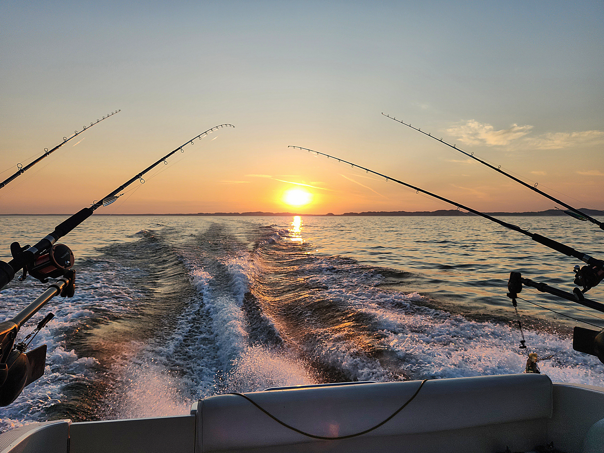 Fishing poles on a power boat with boat wake and sunrise sky over the horizon in Islamorada.
