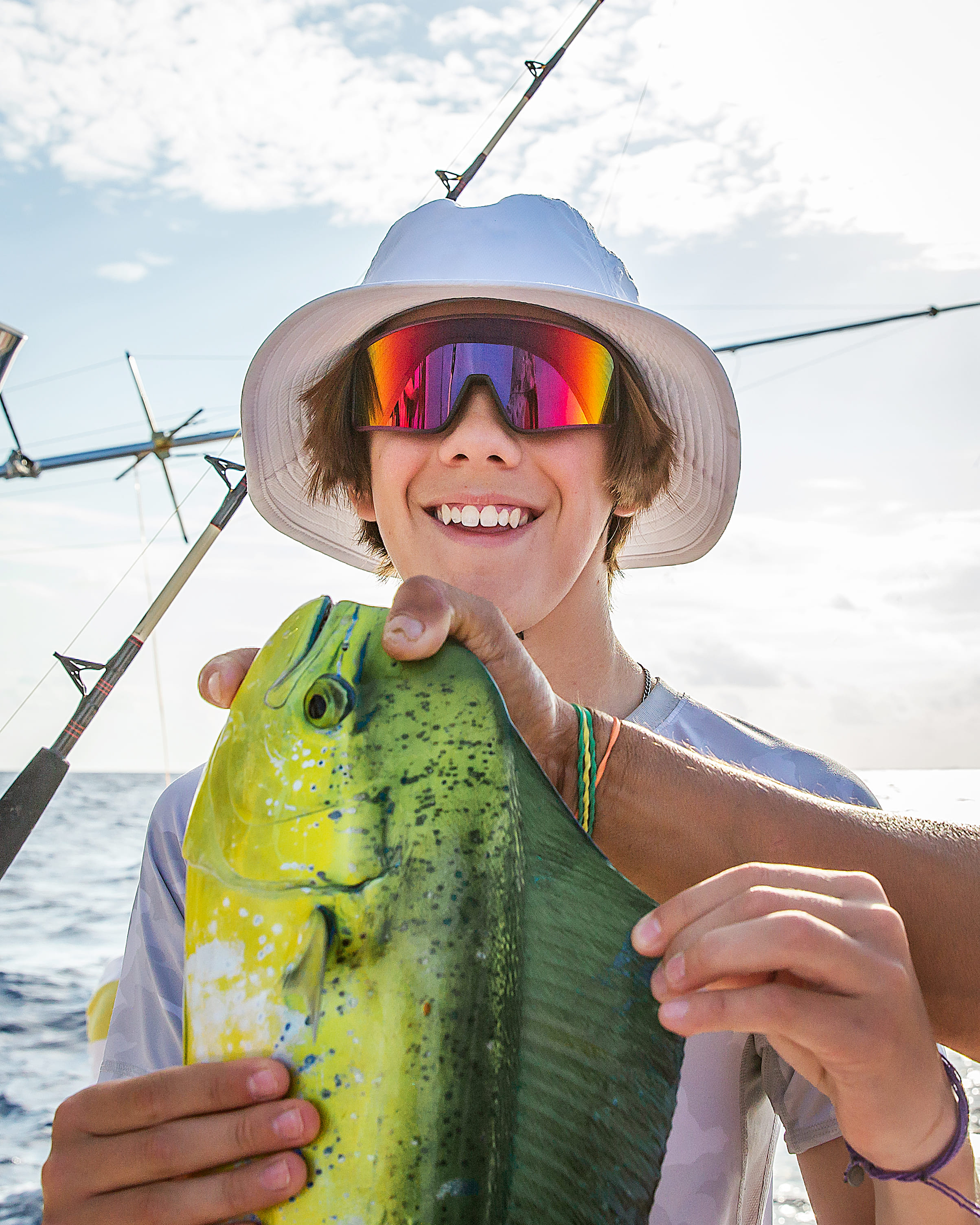 Teenage boy in a white bucket hat with colorful sunglasses holding a green and yellow Mahi Mahi caught off the coast of Islamadora.