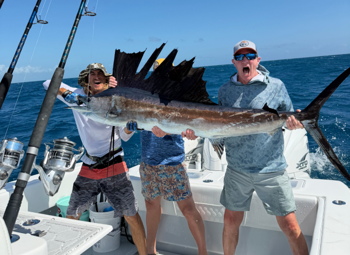 Three men on an Islamorada fishing charter shout and smile in excitement after catching a large sailfish.