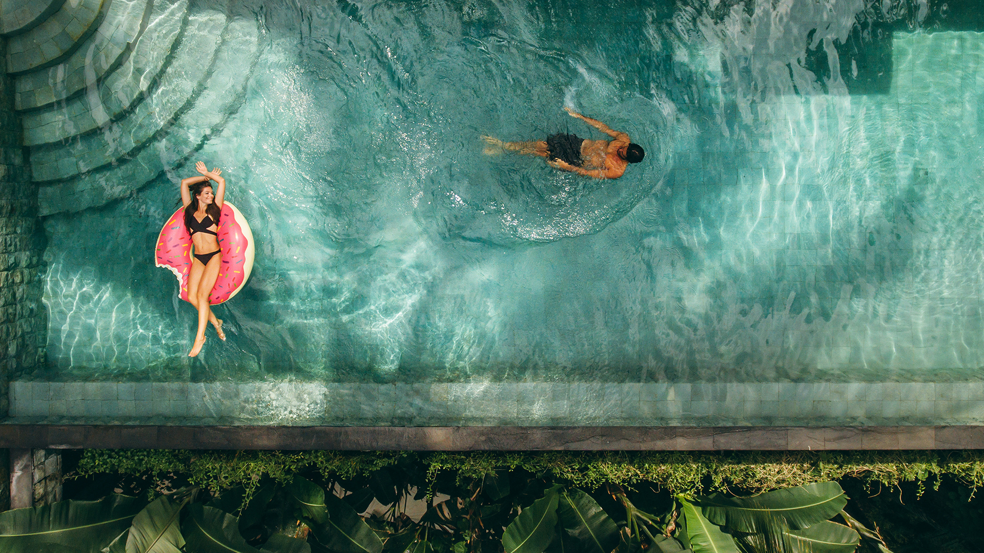 Areal view of a couple people enjoying their time in a swimming pool.