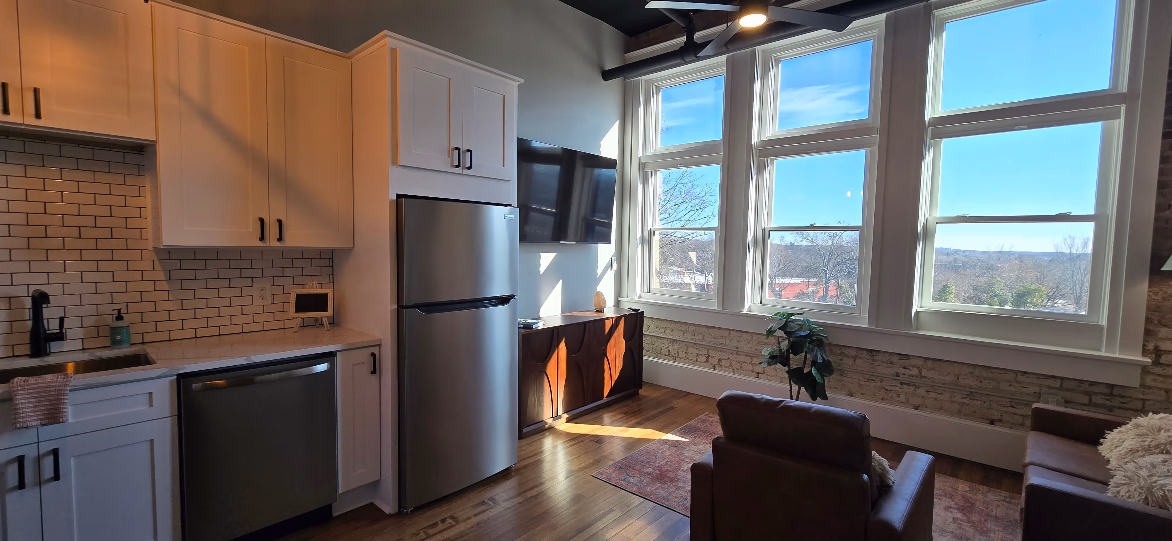 Modern kitchen with white cabinets, stainless steel appliances, and large windows overlooking a scenic outdoor view.