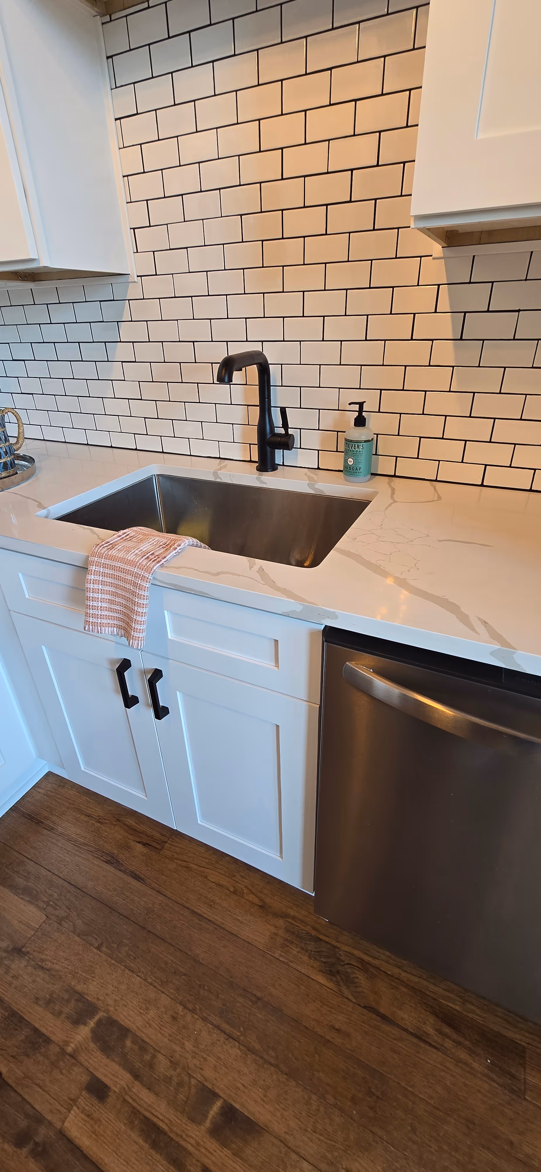 Modern kitchen sink with black faucet, white countertop, subway tile backsplash, and dishwasher below.