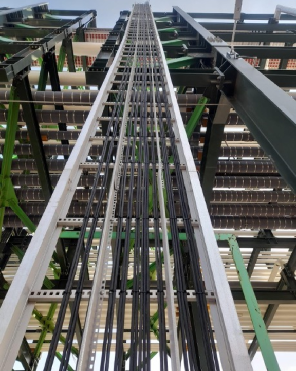 View looking up at vertical metal support structure with multiple black cables running inside an industrial framework.