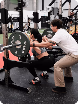 Physiotherapist assisting patient doing weighted barbell squats in a Vancouver physiotherapy clinic.