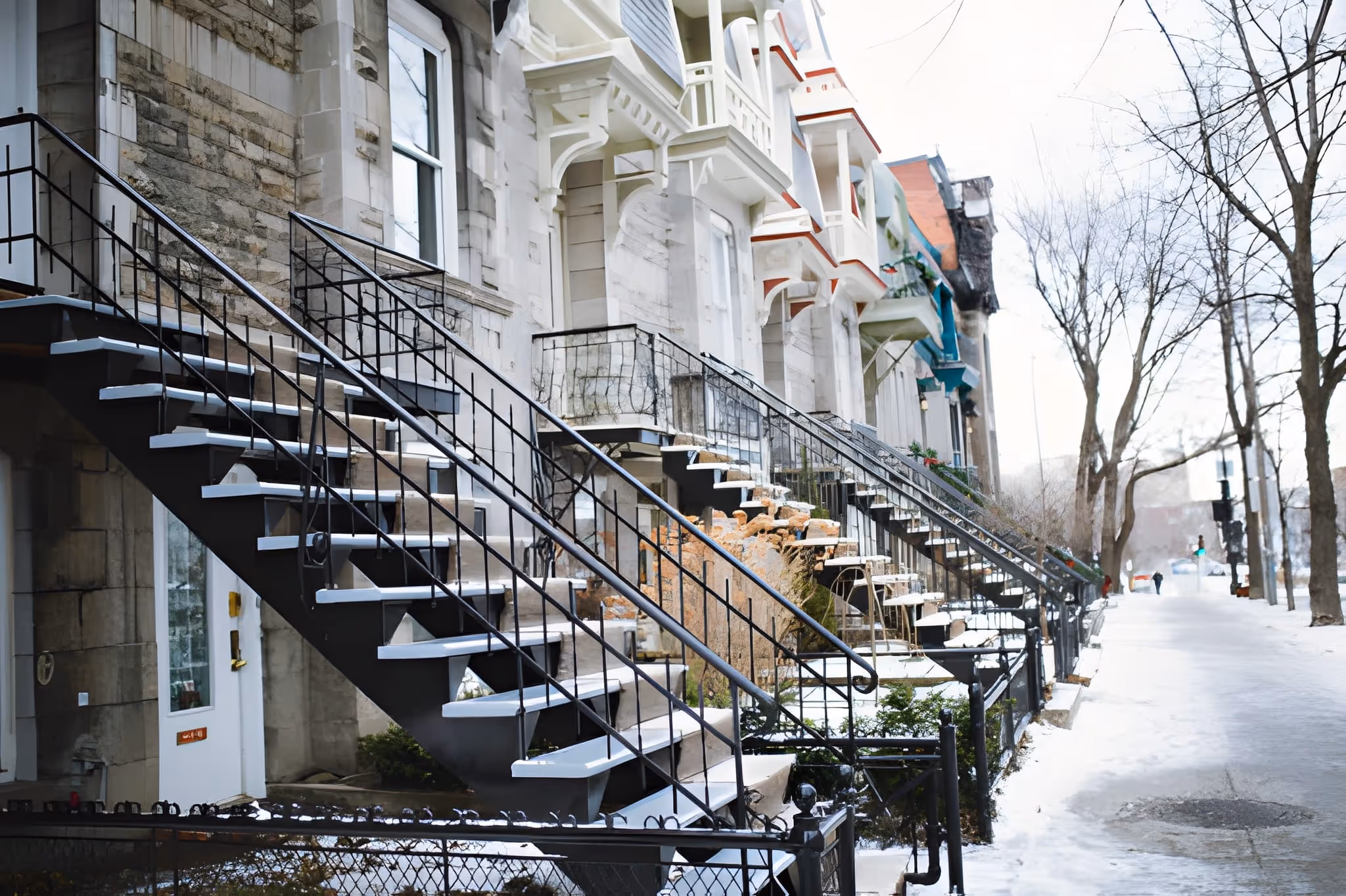 Row of urban townhouses with black metal spiral staircases and snow-covered sidewalks.