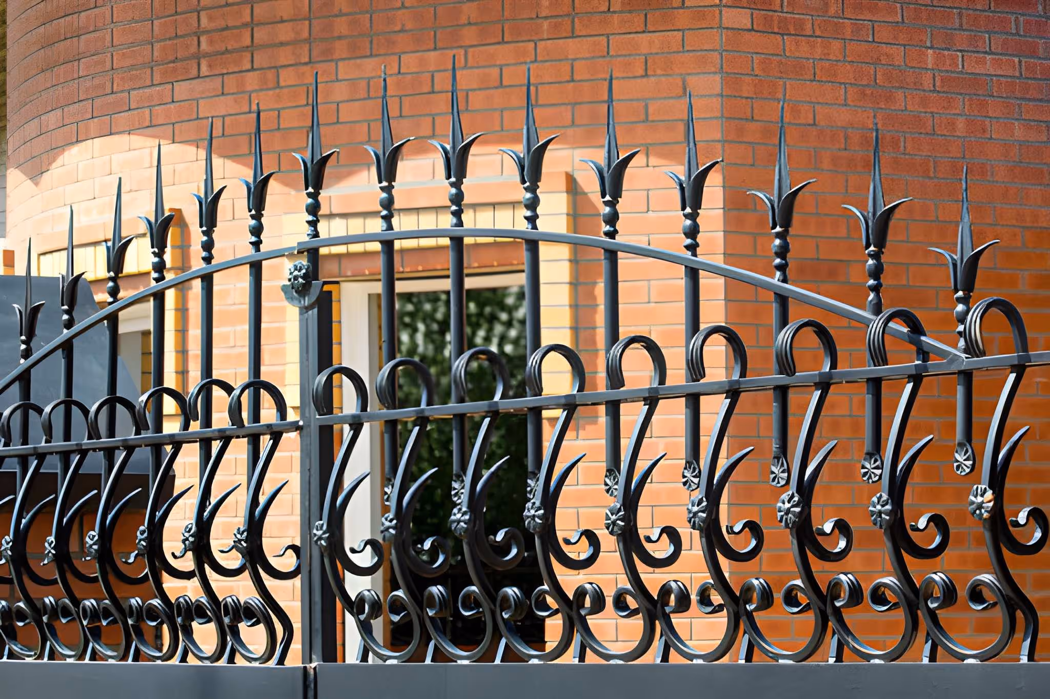 Clôture en fer forgé noire avec des motifs décoratifs devant un bâtiment en briques rouges avec une fenêtre.