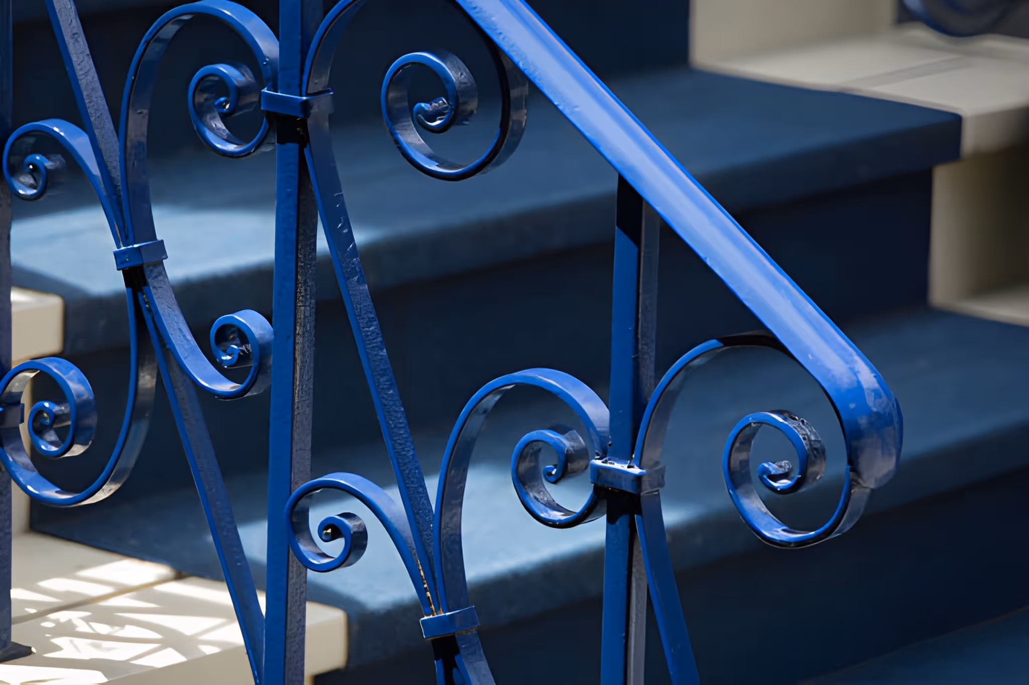 Rampe d'escalier en métal bleu avec motifs en spirale devant des marches bleu foncé.