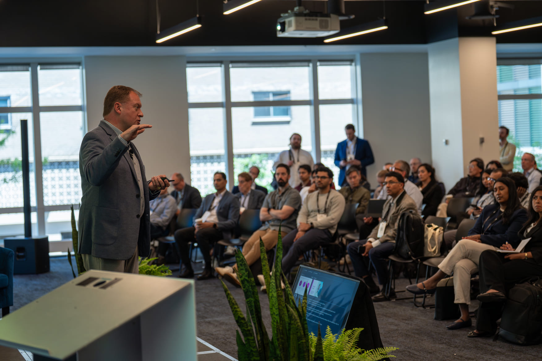 Man giving a presentation to a seated audience in a modern conference room with windows.