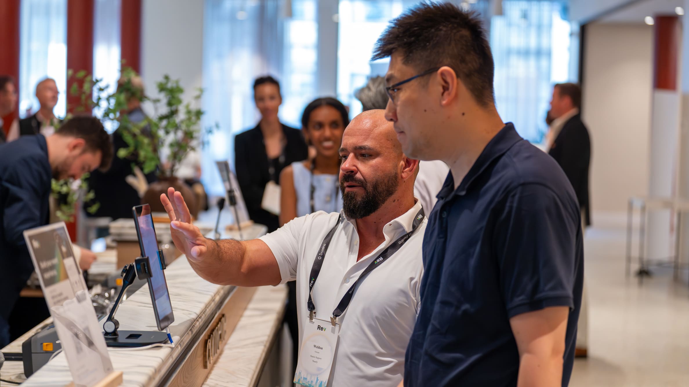 Two men interacting with a touchscreen device on a marble counter at a professional event.