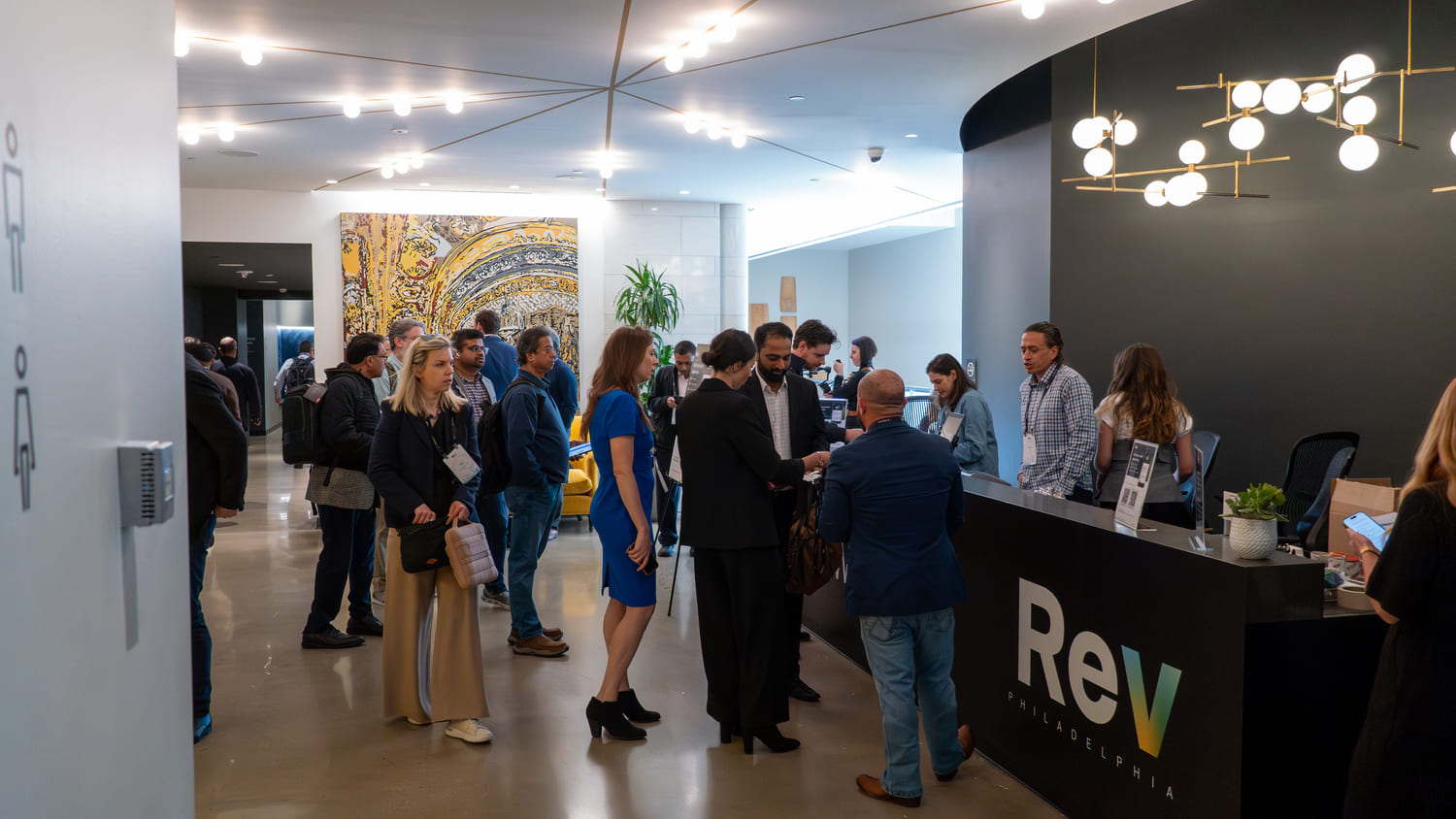 People standing and talking in a modern office lobby near a reception desk with Rev Philadelphia logo.
