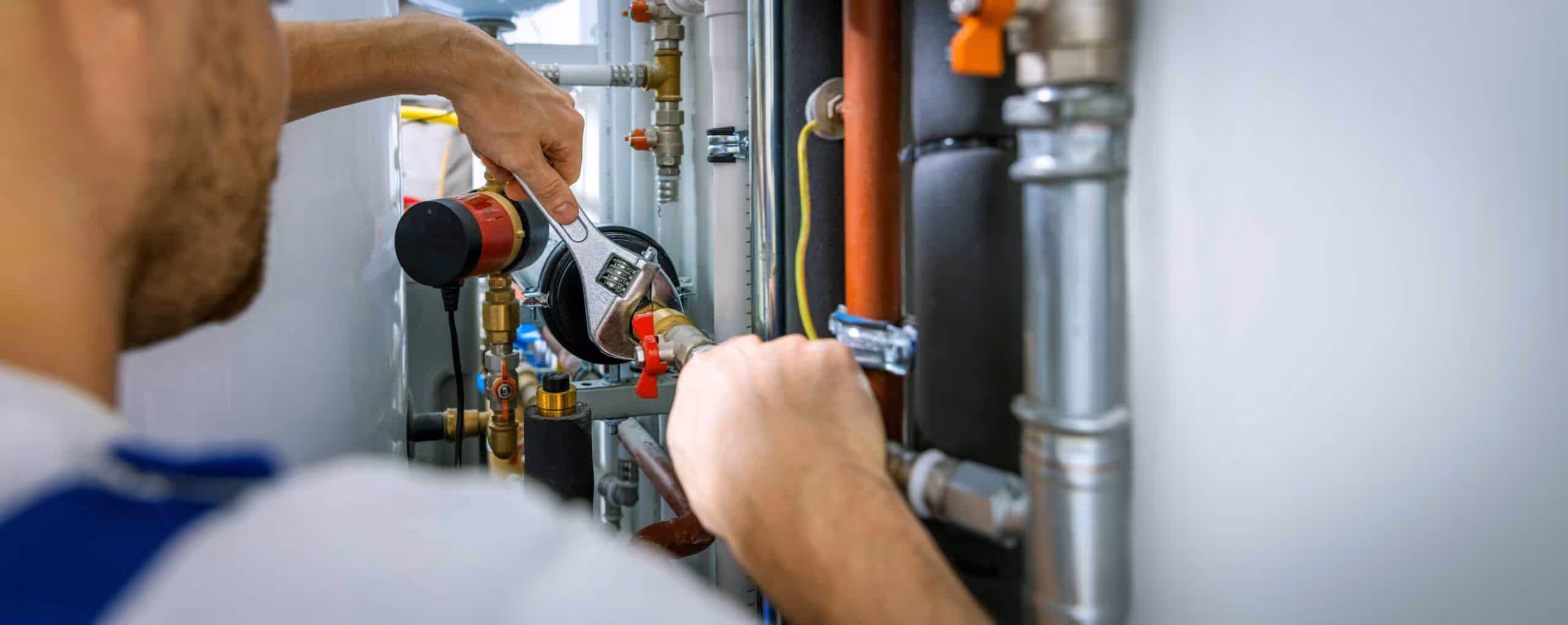 Plumber using an adjustable wrench to fix pipes and valves in a utility room.