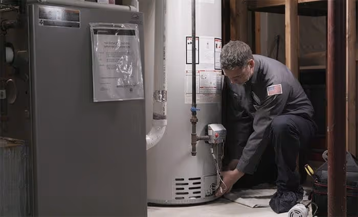 Technician in uniform inspecting and adjusting a water heater in a basement.