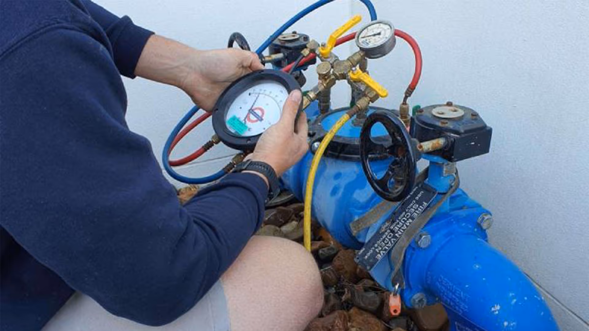 Technician adjusting pressure gauges on a blue water valve system with connected colored hoses.